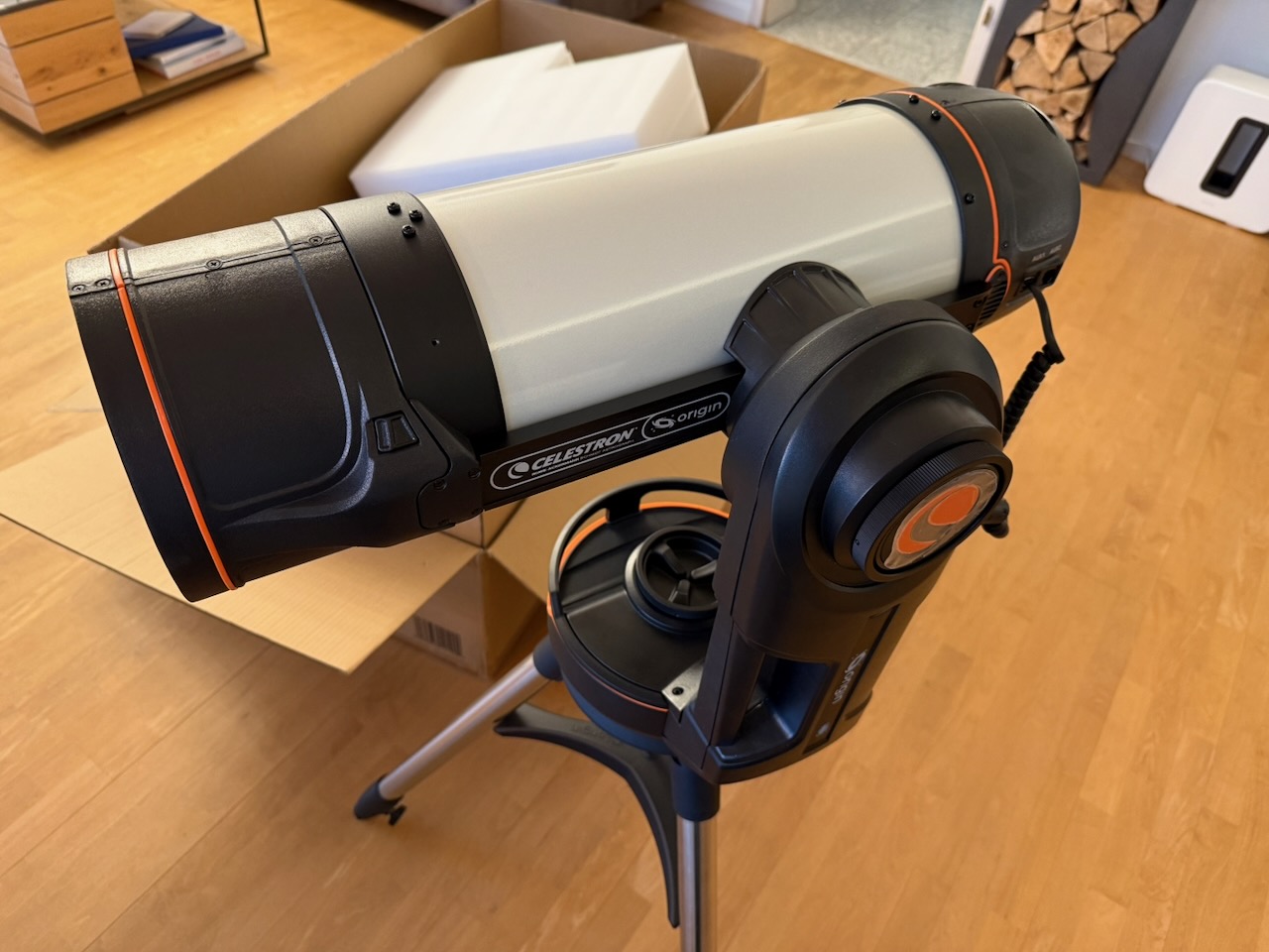 High-tech Celestron telescope setup on tripod in room, with cardboard box and wood flooring background.